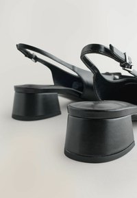 Svart slingback-skor med rund blockklack, slätt lädermaterial och en enskild spänne i remmen.