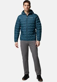 Turkusowa ocieplana kurtka z kapturem, z zasuwakiem i teksturowaną powierzchnią. W zestawie z szarymi spodniami. Doskonała do aktywności na świeżym powietrzu.