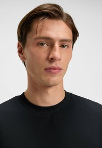 Black circular-neck top made of smooth fabric, fitted design, no visible patterns, focus on the collar and face in a neutral background.