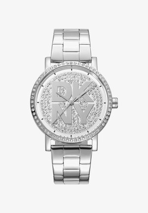 Orologio in metallo argentato con quadrante rotondo, brillanti accenti in cristallo e un prominente logo "DKNY" inciso al centro. Bracciale lucido in stile a maglie.