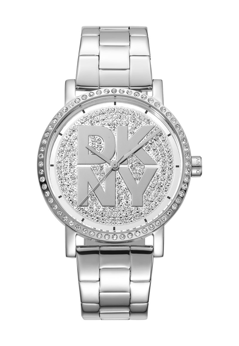 Montre en métal argenté avec un cadran rond, des accents en cristal scintillant et un logo "DKNY" gravé au centre. Style de bracelet en maillon brillant.