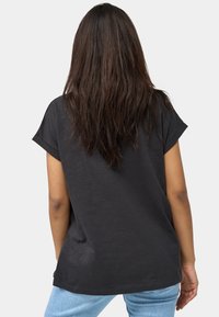 Camiseta negra de manga corta con un corte relajado, textura suave y dobladillo redondeado. La vista trasera muestra mangas ligeramente enrolladas y un diseño de longitud media.
