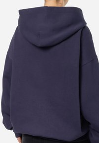 Jakna oversized tamnoplave boje od mekanog materijala, s velikom kapuljačom, spuštenim ramenima i rebrastim manžetama i donjim rubom.