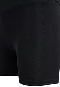 Mustat urheilushortsit, jotka on valmistettu joustavasta kankaasta ja joissa on litteät saumat sekä tiukka istuvuus. Sileä pinta ilman näkyviä kuvioita.