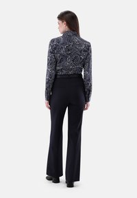Blusa a maniche lunghe di colore blu navy con motivo paisley e colletto alto, abbinata a pantaloni neri a palazzo. La blusa presenta intricate fantasie a spirale.