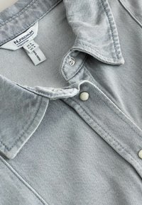 Col du chemise en denim gris clair avec boutons-pression, affichant l'étiquette de la marque "N. Premium Collection" et les étiquettes de taille à l'intérieur du col.