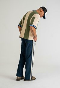 Pulover supradimensionat cu dungi multiple în verde măsliniu și bej, cu accente albastre. Asortat cu pantaloni din denim albastru cu dungi laterale. Încălțăminte maro.