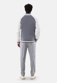 Grauer Cardigan mit weißen Ärmeln, gerippten Bündchen und gestreiftem Detail, kombiniert mit hellgrauen karierten Hosen und weißen Sneakers.