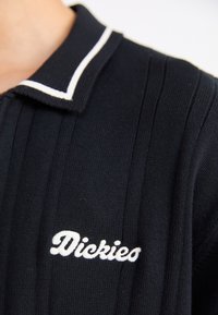 Polo shirt nero a coste con colletto accentato bianco. Presenta il logo ricamato 'Dickies' in bianco nella zona del petto. Texture in maglia morbida.