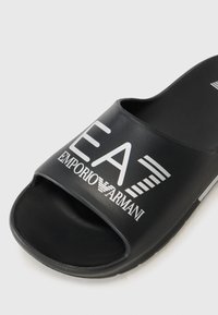 Black slide sandal with a textured rubber sole and wide strap. Features white branding "EA7 EMPORIO ARMANI" prominently displayed.