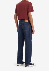 Mörkblå denimjeans med rak passform, med en klassisk femficksdesign och en beige läderpatch på midjan. I kombination med en vinröd t-shirt.