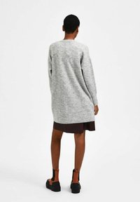 Grey knitted oversized sweater with long sleeves, solid texture, worn over a dark dress, paired with black and brown ankle boots.