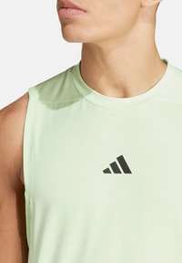 Maglietta atletica verde chiaro senza maniche con colletto rotondo e logo Adidas nero. Tessuto morbido e liscio con una vestibilità aderente per il massimo comfort.
