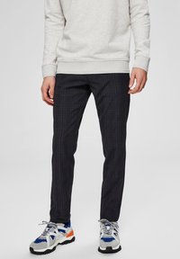 Černé kostkované kalhoty z lehké látky se štíhlým střihem. Kombinovány s bílými a modrými teniskami a světlě šedou mikinou.