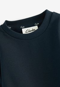 T-shirt blu scuro con colletto rotondo e colletto a costine. Presenta il logo "Clarks" sull'etichetta interna. Realizzato in tessuto morbido e elasticizzato.