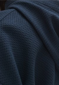 Tessuto blu scuro con una trama goffrata a nido d'ape, drappeggiato in morbide pieghe che creano ombre e profondità.