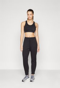 Black sports bra with Champion logo, paired with black jogger pants featuring drawstring and ribbed cuffs, worn with gray athletic shoes.