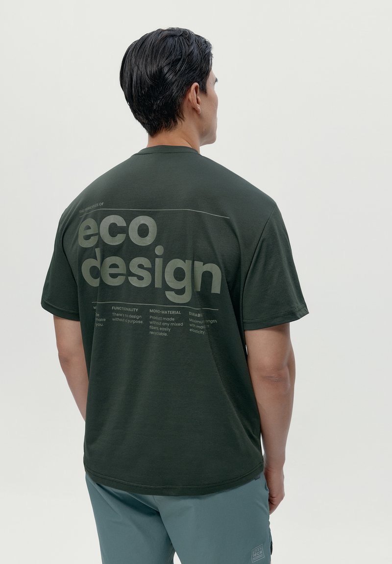 Temno zelena majica s sproščenim krojem, ki prikazuje besedilo "eko oblikovanje" v beli barvi, ter oznake s podrobnostmi o načelih trajnosti na hrbtni strani.