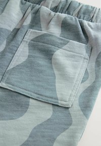 Világoskék és szürke álcázó rövidnadrág, rugalmas derékkal, egy cipzáros zsebbel és sima szövettextúrával.