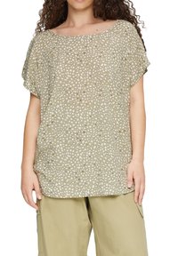 Losse blouse van lichtgewicht stof, met een olijfgroene basis en een wit stippenpatroon, en een brede, ronde halslijn.