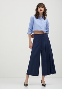 Camicia blu a righe cropped e culotte blu navy a vita alta con pieghe frontali. Tacchi neri completano il look. Tessuto liscio, vestibilità su misura.