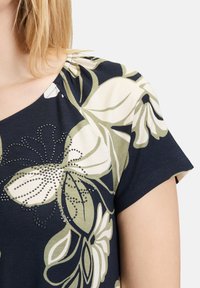 T-shirt met korte mouwen en bloemenprint, met een marineblauwe achtergrond, groene en crèmekleurige bloemen, en accenten van zilveren rhinestones.