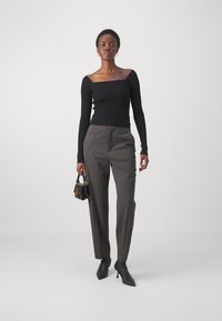 Haut noir à manches longues côtelé avec un décolleté carré, associé à un pantalon gris ajusté et des bottines noires à talons, tenant un petit sac noir.