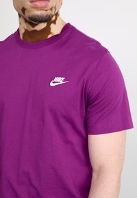 Lila bomulls t-shirt med korta ärmar och rund halsringning. Vit Nike-logga på vänster bröst. Slät textur, avslappnad design.