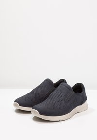 Tengerészek slip-on cipők, perforált velúrból készültek, világos színű gumitalppal, rugalmas oldalsó panelekkel és sima felülettel.