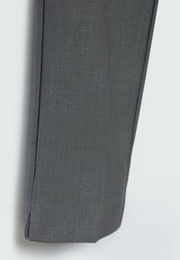 Gros plan sur une jambe de pantalon sur mesure gris foncé avec une couture visible et une petite fente au bas sur un fond clair.