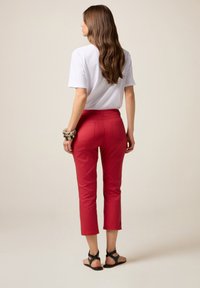 Pantalons rouges courts avec une coupe ajustée, dotés de poches arrière et d'une texture lisse. Associés à un t-shirt blanc uni et des sandales noires.