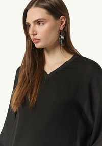 Black, lightweight blouse with a V-neckline and short sleeves. Model wears shiny circular earrings, hair cascading over shoulders.