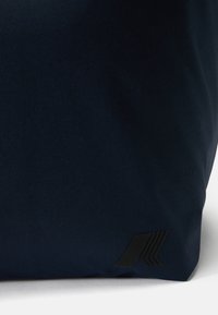 Marinefarget totebag i stoff med en matte svart logodetalj. Har en myk tekstur og en strukturert form, egnet for uformell bruk.