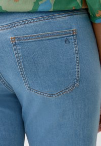Jeans de mezclilla azul claro con un solo bolsillo trasero, con costuras en naranja a contraste y un pequeño logotipo en forma de triángulo sobre el bolsillo.