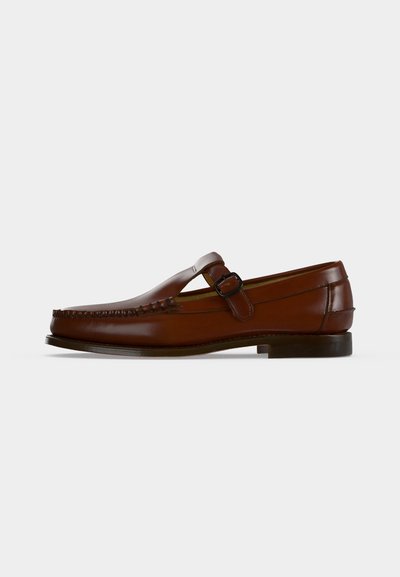 Mocassin en cuir marron avec une bride latérale à boucle et un petit talon sur un fond blanc uni.