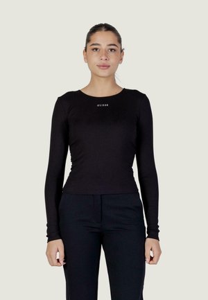 Top a maniche lunghe nero in tessuto a coste con scollo rotondo e logo "GUESS" bianco sul petto. Abbinato a pantaloni neri.