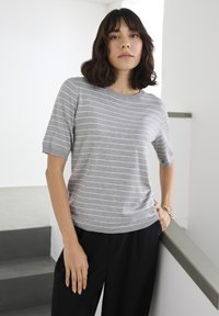 Hallikas lühikeste varrukatega t-särk valgete horisontaalsete triipudega, lõdva lõikega ja ümara kaelusega. Sobitatud mustade lahtiste pükstega.