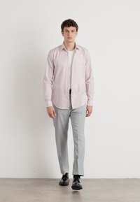 Helles rosa Knopfhemd mit einem gepflegten Kragen, kombiniert mit maßgeschneiderten hellgrauen Hosen und schwarzen Schuhen. Glatte Stoffqualität, schlanker Schnitt.