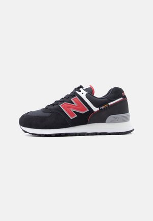 Baskets New Balance noires et rouges avec une semelle intermédiaire blanche, une semelle extérieure noire et une étiquette en tissu Cordura sur le côté.