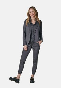 Gray two-piece outfit featuring a tailored blazer and elastic waist pants. Glossy black shoes and a buttoned shirt complete the look.