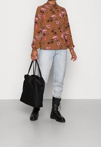 Braun-blusiger Blumenoberteil mit gerafftem Kragen, hellblaue Jeans, schwarze Kampfstiefel und eine schwarze Tragetasche. Gesamtcasual-Outfit-Design.