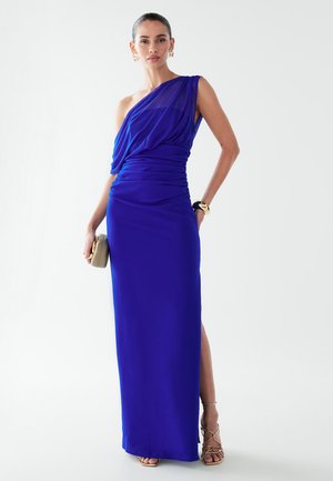 Vienkārša pleca royal blue kleita ar drapētu audumu, sānu šķēlumu un savilktām detaļām; modele tur gaismas krāsas somiņu.