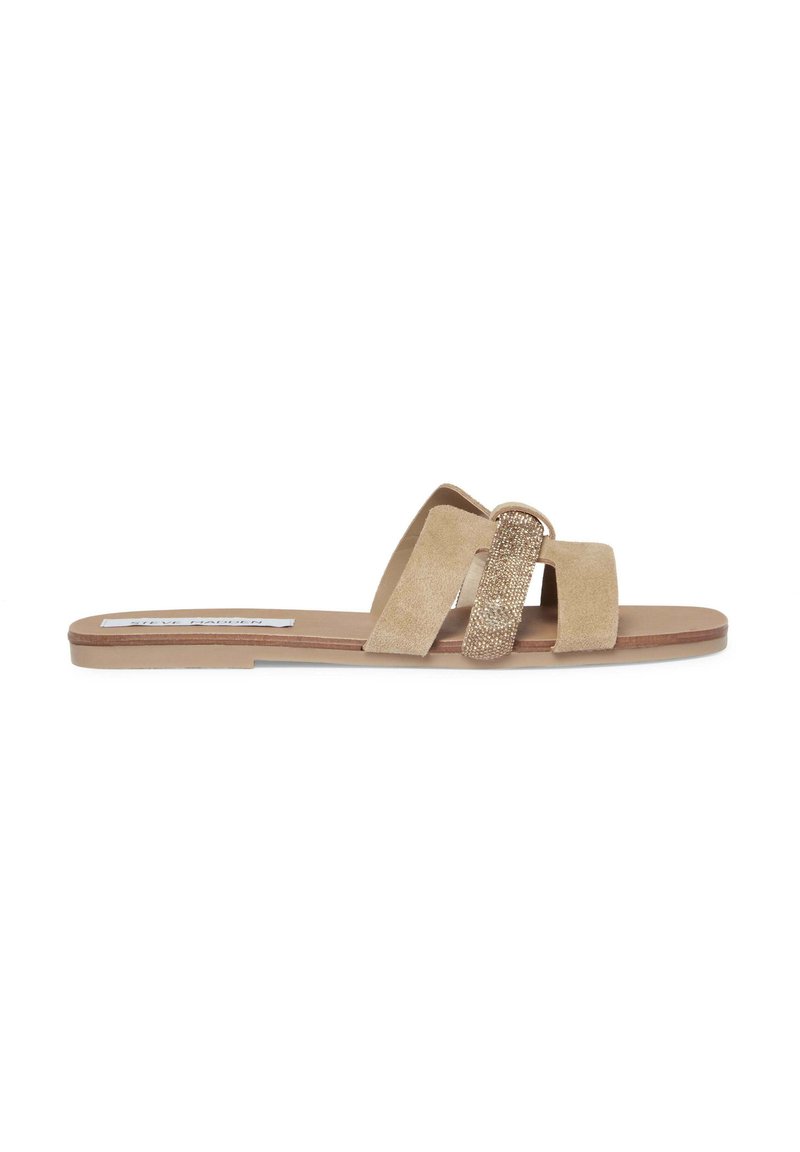 Sandale à glissière en suède beige avec deux brides croisées et un grand accent en métal doré étincelant. Semelle plate avec une finition lisse.