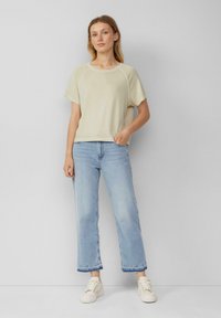 T-shirt a maniche corte color beige chiaro con colletto rotondo, abbinato a jeans a gamba larga blu chiaro. Sneakers bianche completano l'outfit.