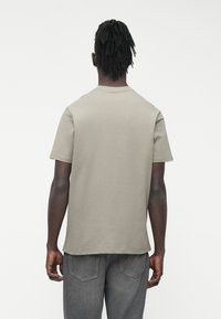 Īsroku krekls no gaiši pelēkas kokvilnas ar apaļu apkakli un brīvu piegriezumu, gludu tekstūru un bez redzamām rakstām.