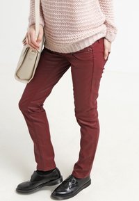 Bordeaux slimfit byxor med en mjuk textur, med framfickor och stickade detaljer. Matchas med svarta slip-on skor och en beige väska.