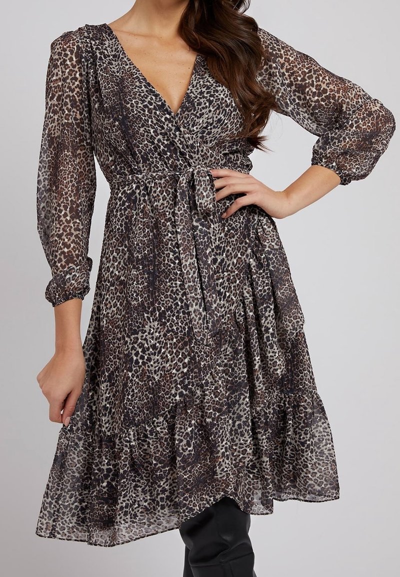 Femme portant une robe portefeuille transparente à imprimé léopard avec des manches bouffantes trois-quarts et une ceinture en tissu nouée à la taille.