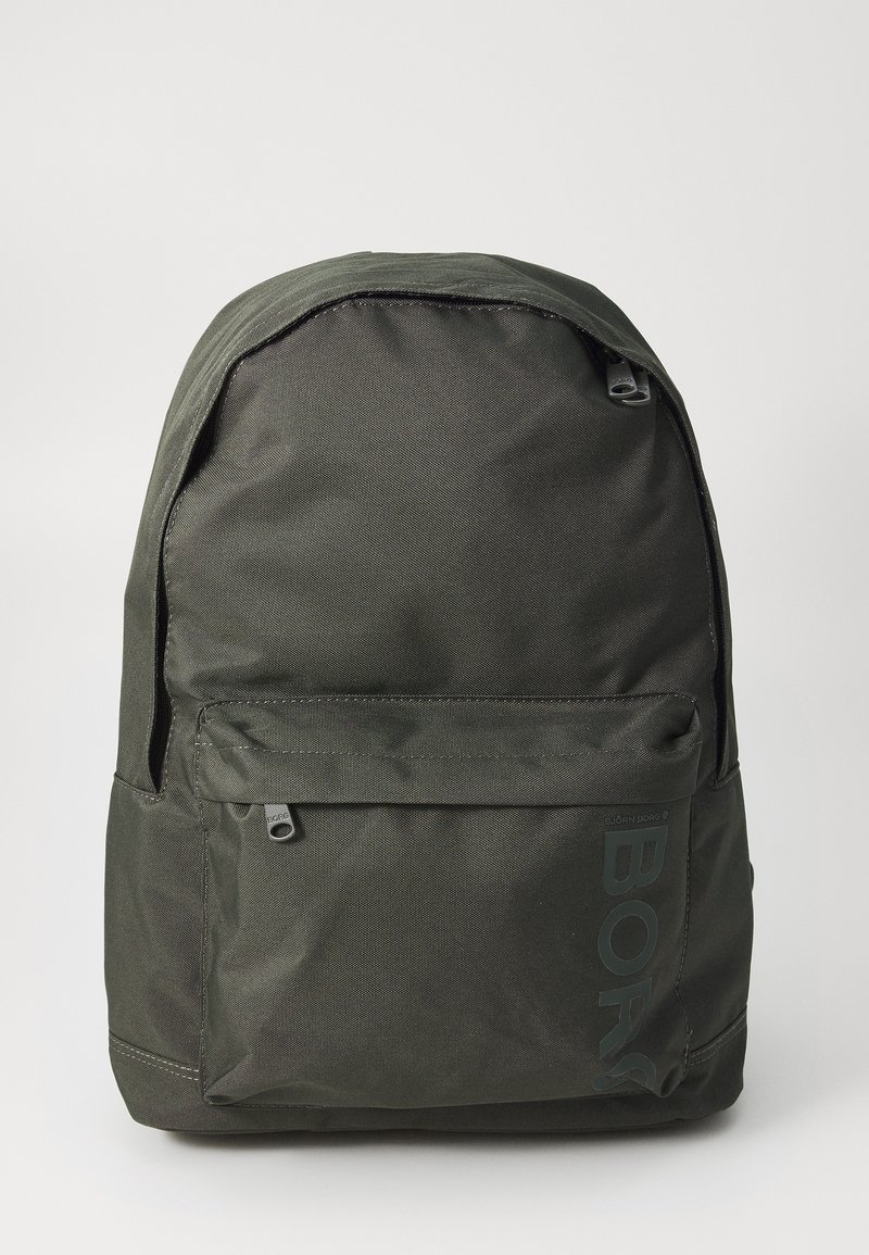 Mochila verde escura com exterior em nylon texturizado, forma arredondada, bolso frontal com fecho e um grande logotipo impresso na lateral.