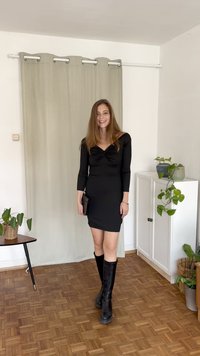 Černé přiléhavé šaty s dlouhými rukávy a výstřihem do srdce, doplněné černými kozačkami po kolena. Jednoduchá, hladká látka; bez vzorů.