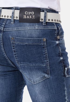 Dunkelblaue Jeans aus Denim mit einem ausgewaschenen Finish, ausgestattet mit silbernem Beschlag, dekorativen Nähten und einem schwarz-weißen gemusterten Gürtel.